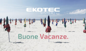 Ampia spiaggia di sabbia bianca con ombrelloni chiusi multicolor e la scritta "Buone vacanze".