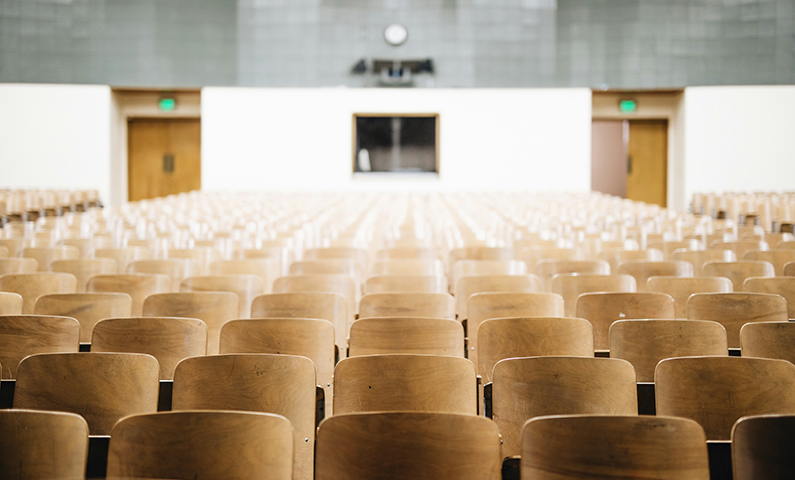 Vista dalla cattedra di un'aula universitaria, con le uscite di emergenza sul fondo, immagine che introduce il tema dell'adeguamento antincendio università.