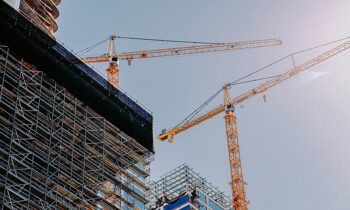 Grande cantiere edile con due grandi edifici in costruzione e due gru, immagine che introduce il tema del badge di cantiere, strumento previsto dal decreto sicurezza sul lavoro 2025.