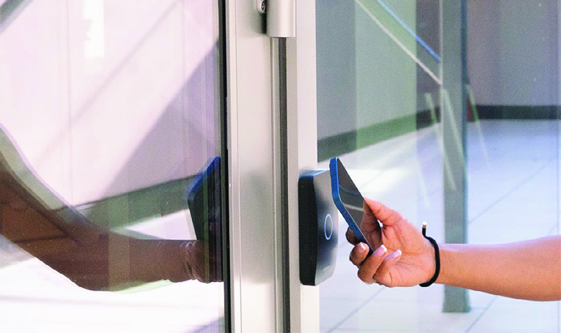 Primo piano di una mano femminile che avvicina il proprio smartphone ad un lettore del sistema di controllo accessi Avigilon.