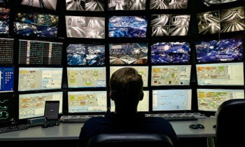 Vista di una sala operativa con un grande monitor suddiviso in tante schermate e un uomo seduto di spalle che svolge un controllo visivo delle riprese delle telecamere. L'immagine introduce l'articolo sulle tecnologie AcuSeek e AcuSearch di Hikvision.