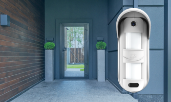 Rivelatore volumetrico per esterno Aris Video CTW di Combivox in primo piano e, sullo sfondo, porta di ingresso vetrata di una villa che lascia intravedere un giardino all'interno.